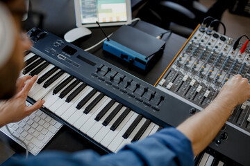 composer hands on piano keys in recording studio. music production technology, man is working on pianino and computer keyboard on desk. close up concept. © Vlad