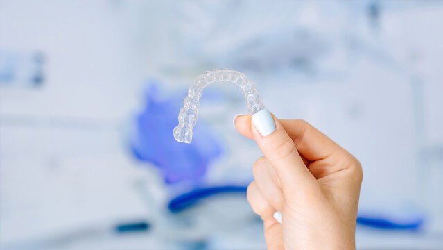 Close-up of a hand holding a clear dental aligner against a blurred background