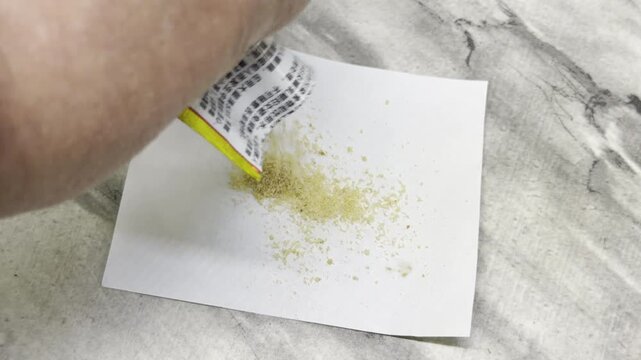 A hand carefully shakes out yellow insect bait powder onto a white sheet of paper. The simple, deliberate action brings a feeling of careful preparation and clean relief.