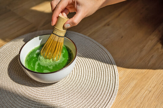 A hand whisking vibrant matcha green tea with a bamboo whisk in a ceramic bowl