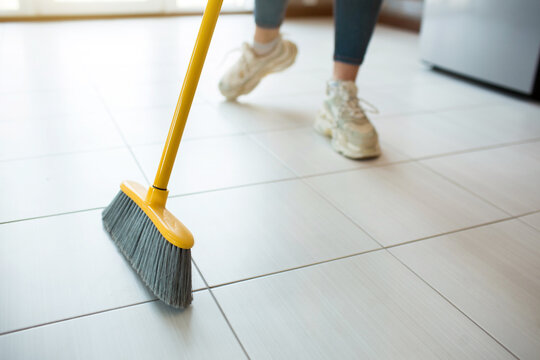 Young woman on kitchen during quarantine. Low cut view of girl in sneakers sweep the floor alone. House holding in kitchen. Daylight.