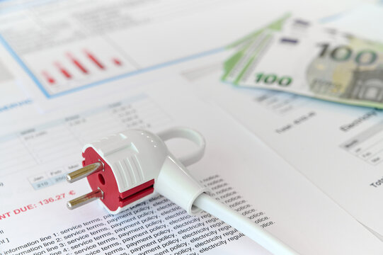 Bills and a bundle of cash lie on a table next to an electric plug, indicating a utility payment situation.