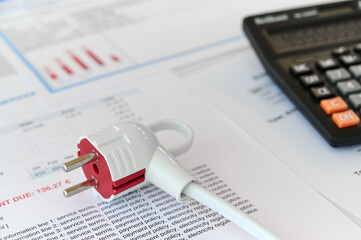 Fototapeta premium A red and white electric plug is on top of service documents with a calculator nearby in an office space