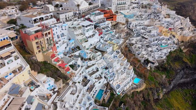 Aerial video looking down at the whitewashed luxury villas, blue pools, and steep volcanic cliffs of Fira, Santorini, capturing the unique island architecture.