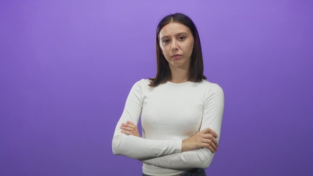 Woman arms crossed with visible hands in studio purple backdrop wearing white long sleeve shirt; disapproval assertiveness.