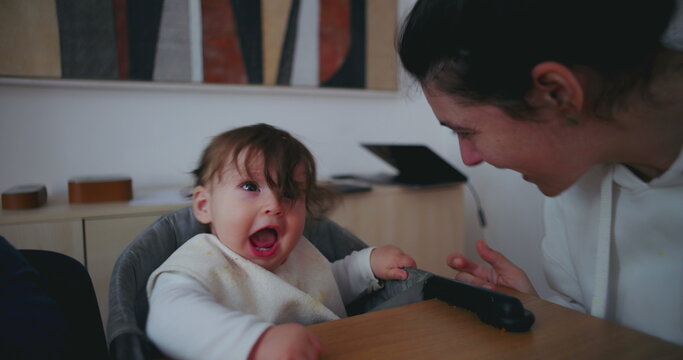 Goofy mom leaning toward baby toddler at dining table being playful and silly expressing authentic family bonding joy love and tender everyday relationship indoors