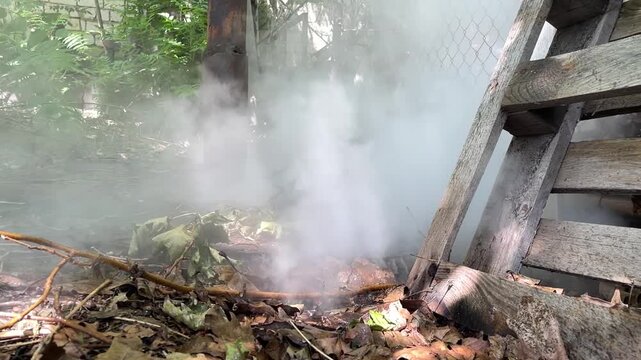 Realistic footage of dense steam rising after hot water pipe rupture near fence and wooden ladder outdoors
