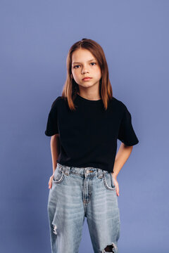 Young girl with medium brown hair wearing a black t-shirt and ripped jeans poses confidently against a solid purple background in a studio setting