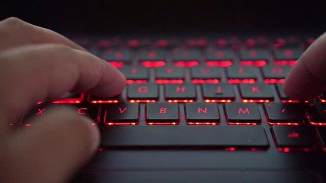 Person typing on backlit keyboard, close-up, digital workspace, technology, and online activity.