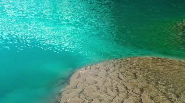 Close-up of vibrant turquoise water in Lake Louise revealing ripple mark patterns in fine glacial silt, shaped by gentle waves in a pristine alpine setting.