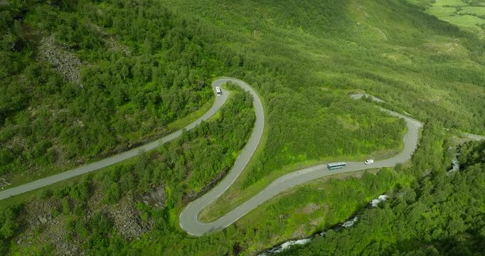 Scenic aerial view of winding hairpin bends in a green mountainous landscape as buses travel along a curving road approaching sharp turns in a serene natural setting.