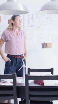 Vertical video: Review starting, lead in pink blouse walking table in studio inspecting turbine