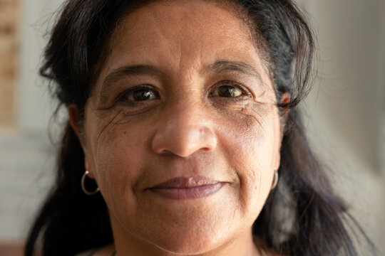 Mature African American woman sitting by window at home, showing skin texture and hoop earrings