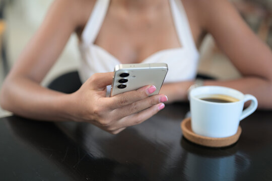 A smartphone and coffee cup held by a beautiful Thai Isan woman in a coffee shop restaurant