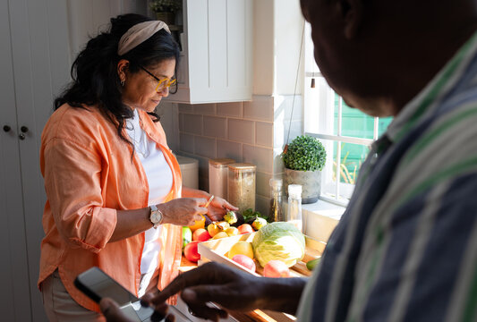 African American couple prepping fruit on kitchen counter tray knife, man holding cell, copy space