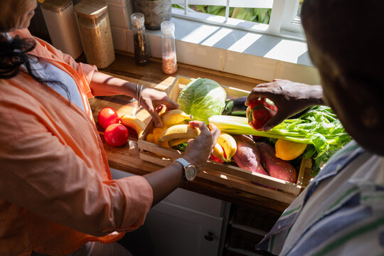 African American couple sorting bananas and peppers at sunny counter with wooden crate and watch