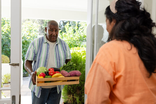 African American couple standing at home doorway, man wearing striped shirt holding wooden crate
