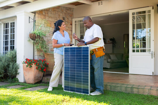 African American homeowner and installer standing on porch inspecting solar panel with screwdriver