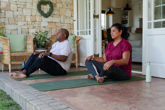 Senior African American couple meditating on porch on yoga mats in workout gear with water bottles