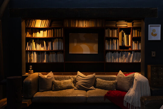 Tan leather sofa sitting in recessed bookshelf reading nook, showing pillows, red throw, spotlights