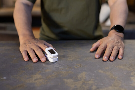 Asian senior man leaning over countertop, checking pulse oximeter while wearing black smartwatch