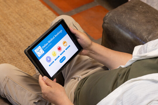Tablet black case is displaying online medical bookings while hands are holding on sofa near tiles