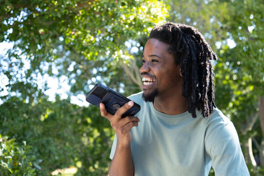 Adult African American man laughing, speaking into phone-bulky-case-grip at park in sage tee