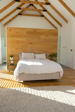 Upholstered bed sitting centered against wood wall, sunlight through blinds casting striped shadows