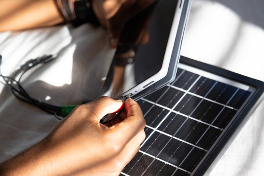 African American man plugging cable into white tablet on solar panel on sunny sheet wearing watch