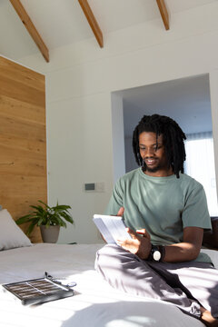 African American man sitting on bed in bedroom using tablet charging with solar panel, copy space
