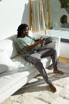 Man reclining on white sectional sofa in living room, holding controller and grid pad