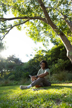 African American man sitting in park wearing T-shirt holding tablet with folio nearby, copy space