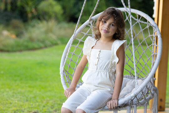African American child sitting in macrame hanging chair on porch with cushion wearing romper