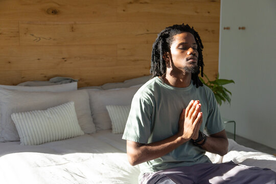 African American man sitting on edge of bed in bedroom wearing wristband, green T-shirt, copy space
