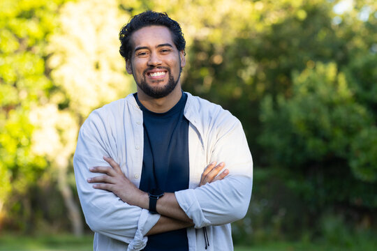 African man standing outdoors in park wearing light buttonup shirt and navy tee, wristwatch visible