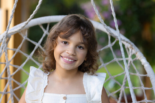 African American girl child sitting in woven chair in garden in sleeveless dress with wood button