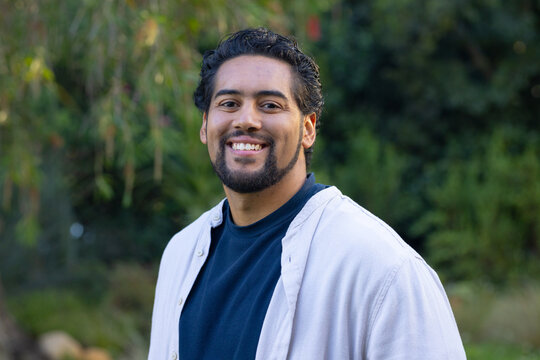 African American man smiling and posing mid-chest up in garden wearing beige overshirt navy T-shirt