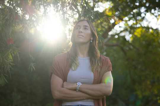 Woman standing beneath tree canopy, looking upward, wearing rust shirt and wristwatch