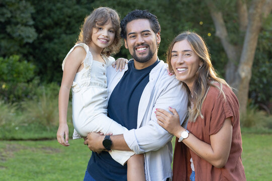 Family posing on park lawn, dad holding daughter, dad wearing smartwatch, mom wearing wristwatch