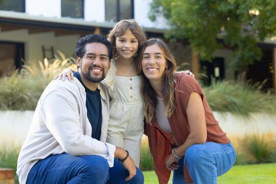 Diverse family of three posing on green lawn in front of house with porch and wristwatch