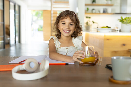 African American child sitting in kitchen holding glass of orange juice with notebook and headset