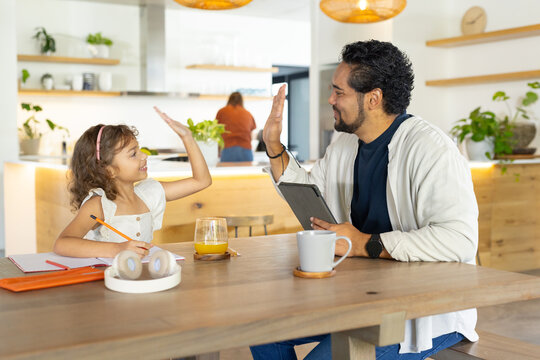 African American father and youth girl sitting at kitchen table high-fiving over tablet, pencil