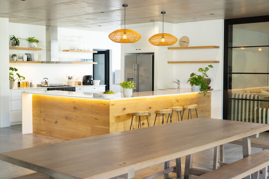 Kitchen island is featuring white countertop and warm LED strip lighting, three stools, fruit bowl