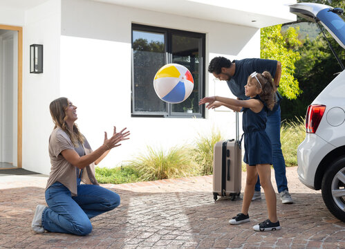Diverse family loading car with suitcase and playing with multicolored beach ball on driveway