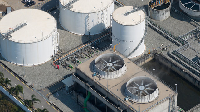 Aerial view of the Amata B.Grimm Power Rayong 5 facility featuring large demineralized water tanks, cooling towers with rotating fans, and industrial piping in Map Yang Phon, Rayong, Thailand.