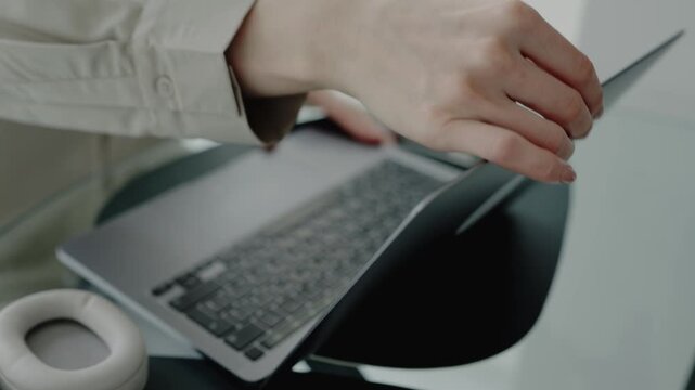 A woman working from home, typing on a laptop at her desk. Headphones are placed beside the laptop, suggesting remote work or studying in a home office setup.
