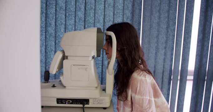 Woman Undergoing an Eye Exam Using Modern Medical Equipment. A focused woman in a relaxed outfit conducts an eye examination using advanced optical diagnostic equipment.