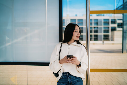 Cheerful girl with braces laughing and looking at phone screen, receiving good news, success and achievement concept, sitting at modern bus stop, urban connectivity, lifestyle photography.