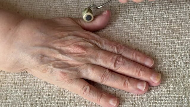 Elderly woman hand close-up rolling silver massager, textured roller with sharp edges gliding over wrinkled skin and knuckles