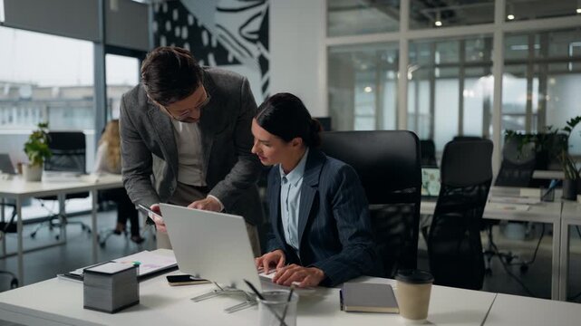Caucasian businesswoman working with laptop businessman coming in office asking help ask advice showing digital tablet two business colleagues discuss job female woman leader consult man male worker